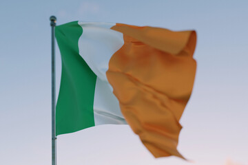 National flag of Ireland waving in the wind against a clear sky, symbolizing patriotism,...
