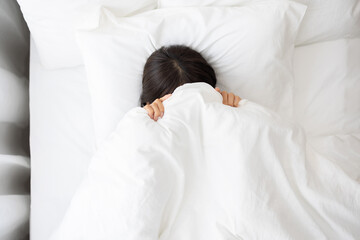Woman Sleeping with Face Hidden Under White Blanket in Bed