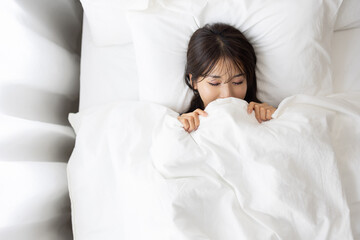 Woman Sleeping with Face Hidden Under White Blanket in Bed