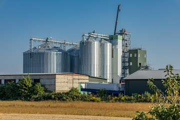 Obraz premium Granary facility features multiple silos for grain storage, located in an agricultural area with open fields and clear weather