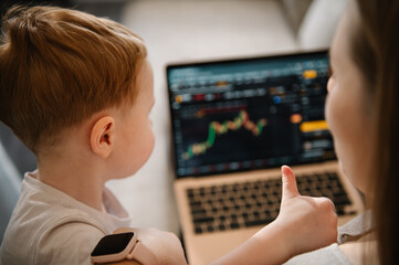 Work cryptocurrency market chart on laptop monitor screen. Kid make noise and disturb woman working talking on phone. Mom work on laptop from home with child. Selling ether, bitcoin or altcoin.