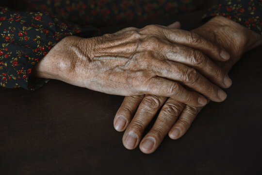 Close-up of wrinkled hands with visible veins resting on table