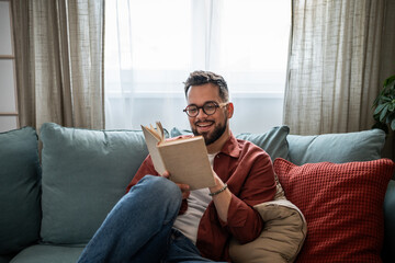 Happy man reading book relaxing on sofa at home