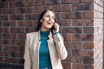 A lively woman smiles as she talks on her phone against a brick wall, exuding confidence and engagement with her surroundings.
