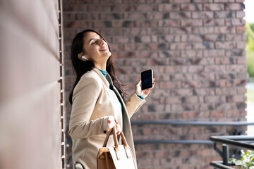 A carefree woman embraces joy as she takes a moment to enjoy her music, highlighting her fashion sense in an outdoor space.