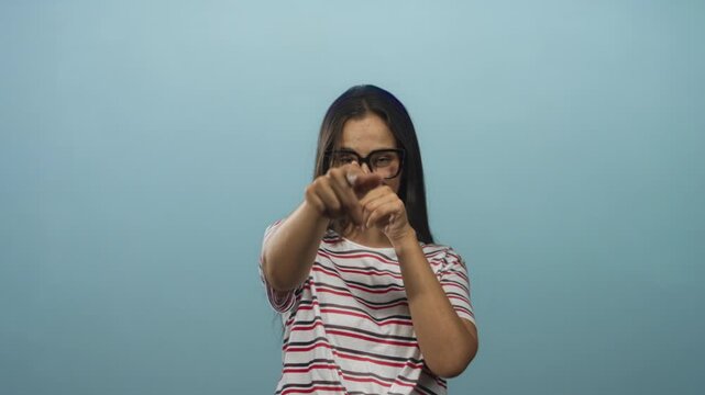 Woman pointing finger at camera with glasses and visible hand in a light blue studio; playful confidence.