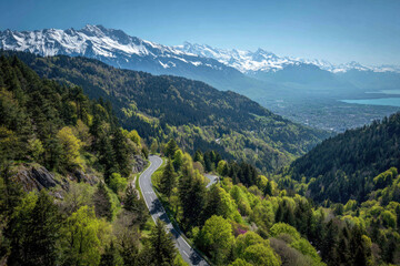Obraz premium Mountain road winds through lush green valley, snowy peaks above