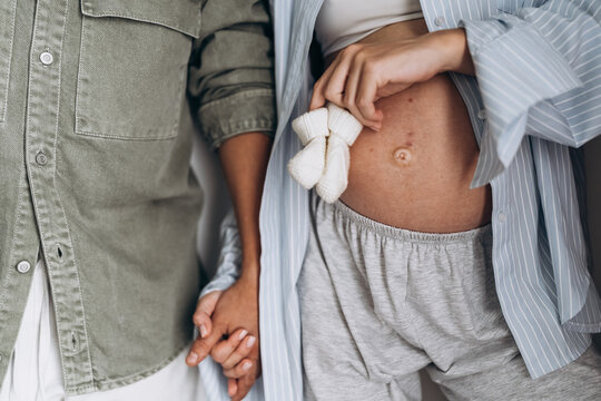 Expectant mother holding baby booties beside partner at home
