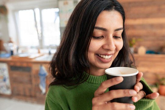 Smiling woman in green sweater enjoying coffee in loft kitchen