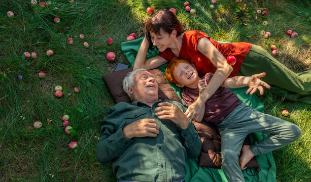 Family enjoying time together lying on grass in garden with apples
