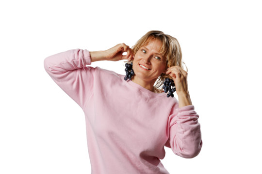 Smiling woman in a pink sweatshirt playfully holds bunches of grapes like earrings, isolated on white background. Fun, quirky concept perfect for healthy or humorous themes