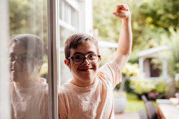 Smiling teenager with glasses and trisomy 21 standing by window outdoors