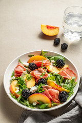 Fresh salad with peaches, arugula, feta, prosciutto and berries in a plate on a light background