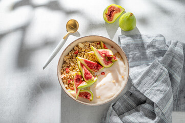 Natural yogurt with granola, figs and honey in a bowl on a light background