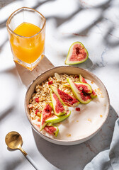 Natural yogurt with granola, figs and honey in a bowl on a marble background