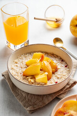 Oatmeal with peaches and nuts  in a bowl on a light background with honey