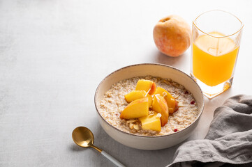 Oatmeal with peaches and nuts  in a bowl on a light background with honey