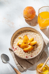 Oatmeal with peaches and nuts  in a bowl on a marble background with honey