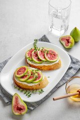 Sweet toasts with fresh figs, cheese, thyme, and honey on a light background.