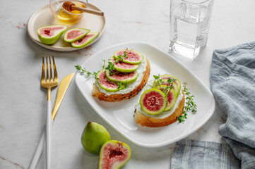 Sweet toasts with fresh figs, cream cheese, thyme, and honey on a marble background.