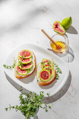 Sweet toasts with fresh figs, cream cheese, thyme, and honey on a marble background.