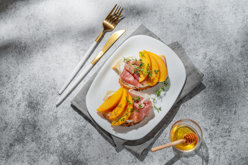 Sandwich with peach, cream cheese, prosciutto and honey on a plate on a gray background