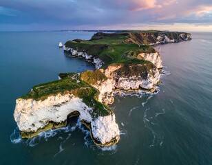 Aerial view of white cliffs with green tops, a natural arch, and a grassy island at sunset