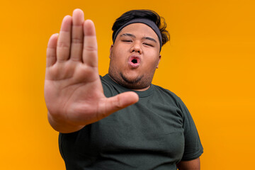 Young Fat Guy in Sportswear Saying No While Showing Palm Hand To Camera Over Yellow Background