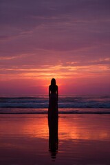 Silhouette of women standing in meditation on the beach shore at sunset.
