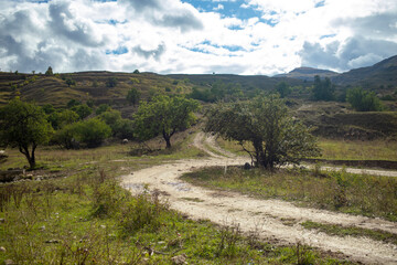Naklejka premium Beautiful summer mountain rural landscape. Panorama of summer green field with dirt road and Sunset cloudy sky. Trekking tourists, camping ground.