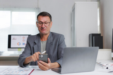 Mature businessman working with smartphone and laptop in office