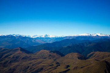 Fototapeta premium Panoramic view of Caucasus Mountains with snow-capped peaks , hills under blue sky. Natural landscape symbolizing freedom, purity, beauty of wild nature. For travel, adventure, eco-tourism concepts.