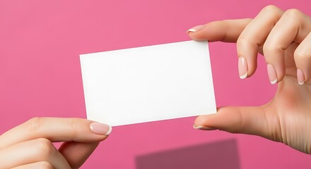Womans hands holding a blank business card against a pink background.