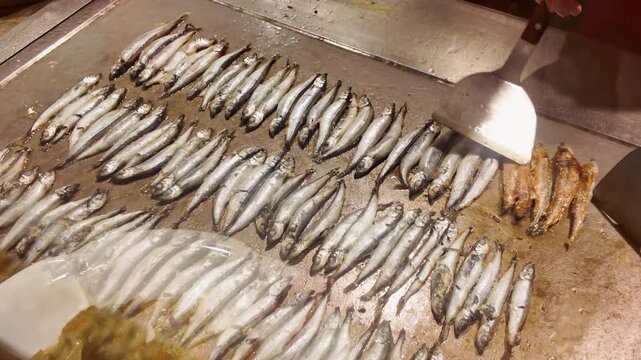 A chef is frying capelin on an iron plate