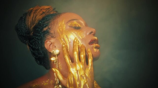 fantasy art portrait lips eyes close up face african american woman. Professional creative golden make-up shiny shadows. Hands in gold liquid drops flow sexy Fashion model beautyl girl. Studio black
