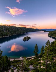 Obraz premium A stunning vista of a calm lake at sunset. Clouds reflect in the still water. Lush forests surround the tranquil water and island