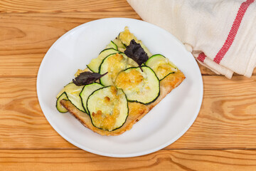 Piece of zucchini pizza on saucer on a rustic table