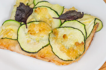 Piece of zucchini pizza on white dish close-up