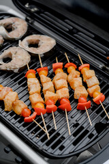 Fish skewers with tomatoes and steaks on a black barbecue grill