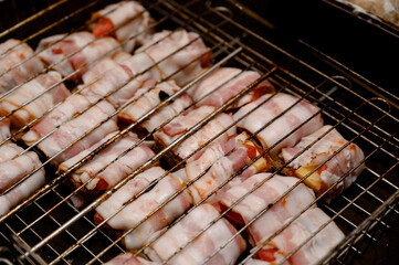 Raw bacon, cheese and bread appetizers arranged on a metal barbecue grill.
