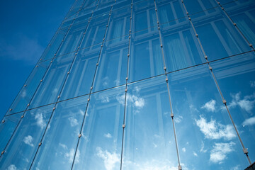 Upward angle view of blue glass skyscraper with reflected clouds and precise metallic grid emphasizing innovation and modern corporate architecture