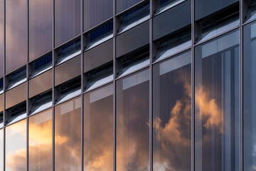 Contemporary office facade with reflections of sunset clouds on glass panels creating warm tones and geometric composition in modern architectural design