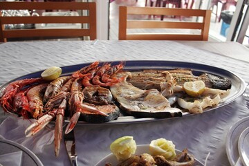 Large platter with grilled fish steaks, whole shrimp and langoustines on a restaurant table. Assortment of fresh and cooked seafood with salmon, white fish, squid and crustaceans with lemon slices
