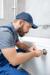 Plumber repairing bathtub faucet with tools in modern bathroom. Plumber tightening fixture near tub 