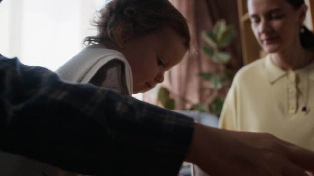 Handheld shot of young Jewish woman sitting at table with her toddler son and husband and having fun together spinning dreidels at Hanukkah at home
