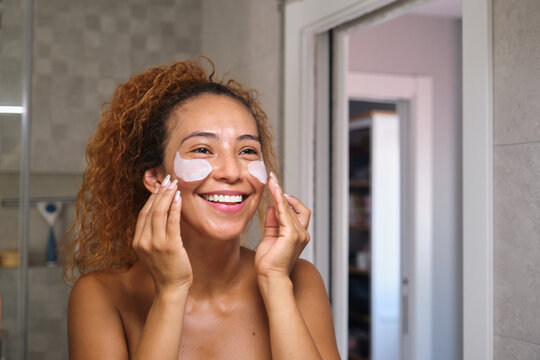 Smiling person applying under-eye patches during skin care routine