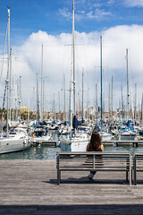Woman contemplates the sailboats at the harbor on a beautiful day, inspiring travel and relaxation while enjoying the peaceful waterfront atmosphere