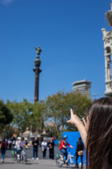 Discovering Barcelona's beauty as a tourist, pointing up at the Columbus Monument with vibrant blue skies during a summer visit, capturing memorable experiences