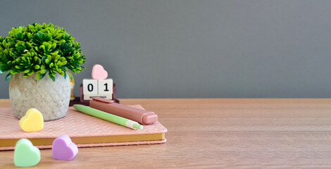 On the wooden surface of the table lies a notebook with a pen, marker, erasers and a calendar. Flower