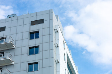 Fototapeta premium A modern building with a curtain-wall ventilated facade made of porcelain stoneware. Clean lines, minimalist style, large windows, a white facade, and balconies with metal railings.